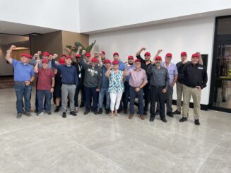 A group of people standing inside an airport. They are wearing red hats, indicating support for airport screening officers.
